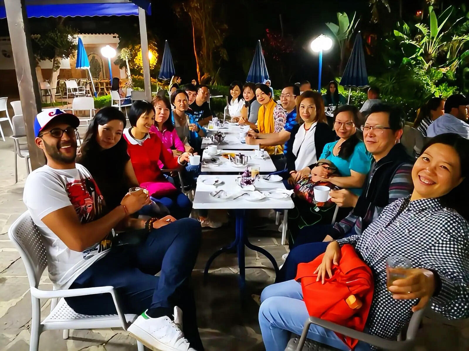Reda Akrime casually dressed with 14 Chinese tourists smiling at a night cafe in Morocco, taking a group photo