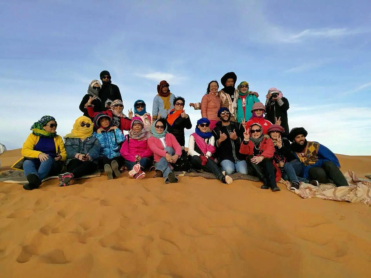 Reda Akrime with 14 Chinese tourists sitting on desert sand in Morocco, taking a group photo